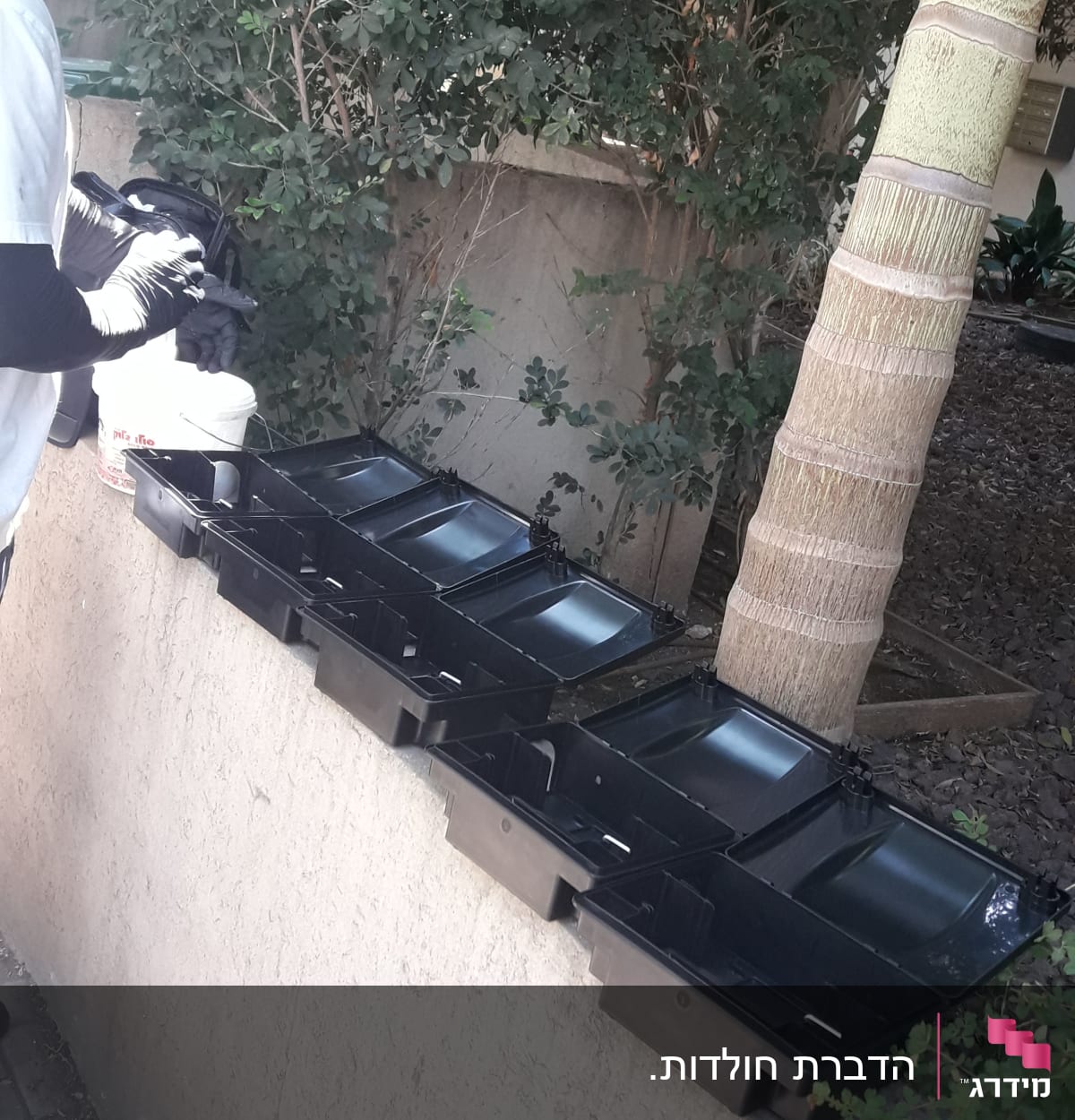 אדם עם כפפות ליד קופסאות הדברה שחורות על קיר